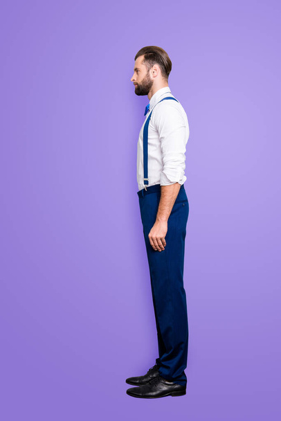 Full size fullbody, profile side view portrait of handsome attractive singer in blue ourfit, wearing bow, white elegant shirt, suspenders, isolated over grey background. - Photo, Image