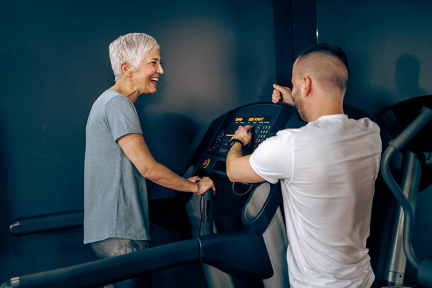 Senior woman is exercising on a treadmill with coach in the gym. - Foto, imagen