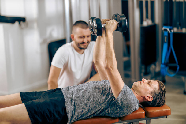 Middle age man is doing training with personal trainer in a gym. - Photo, Image