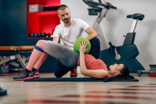 Young woman is doing training for abs with personal trainer in a gym. - Foto, afbeelding