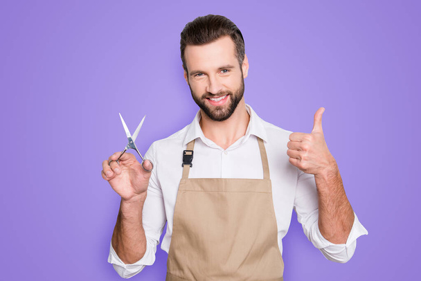 Portrait of cheerful positive barber with stubble in shirt having scissors in hand showing thumb up approve sign with finger, looking at camera, isolated on grey background. - Φωτογραφία, εικόνα