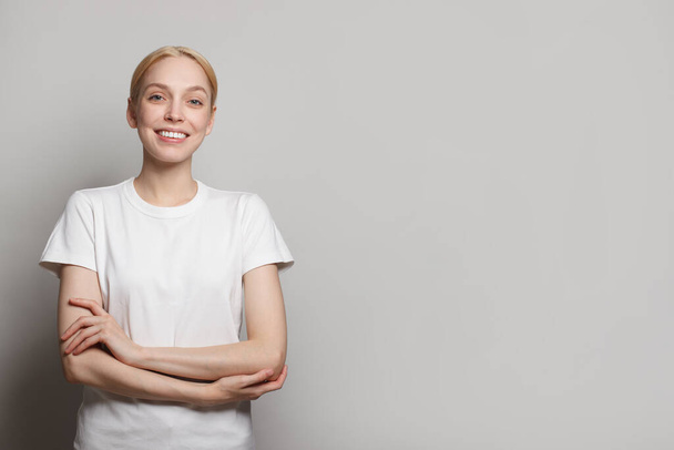 Cheerful young woman wearing white empty t-shirt smiling against white studio wall banner background - Photo, Image