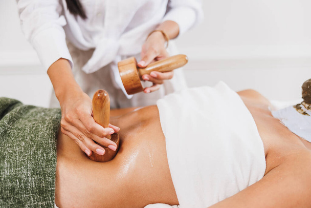 Une femme méconnaissable obtenant un massage anti-cellulite madérothérapie avec une tasse en bois au salon de beauté. - Photo, image