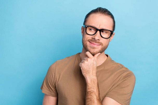 Portrait of cheerful thoughtful guy with long haircut wear khaki t-shirt look at promotion empty space isolated on blue color background. - 写真・画像