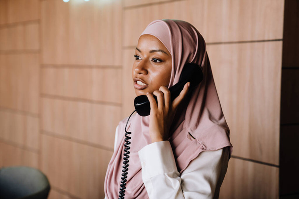 Muslim young businesswoman talking on phone while working at reception - Zdjęcie, obraz