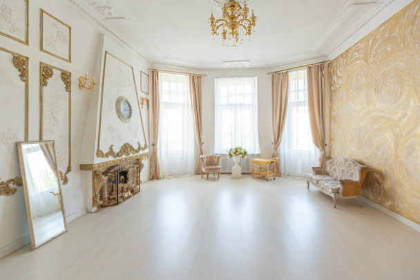 luxurious expensive interior of a large baroque royal living room. antique furniture, gold trim, huge windows, fireplace with gold stucco on the walls. full of daylight - Foto, Bild