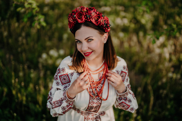 Attractive ukrainian woman in traditional embroidery vyshyvanka dress, ancient coral beads and red flowers wreath. Ukraine, freedom, culture, national costume, victory in war - Photo, Image