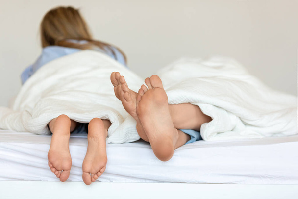Közelkép egy pár lábáról, akik összefonódnak az ágyban, és megragadják a pillanat intimitását.. - Fotó, kép