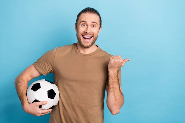 Photo of pretty excited man wear beige t-shirt holding ball thumb empty space isolated blue color background. - 写真・画像