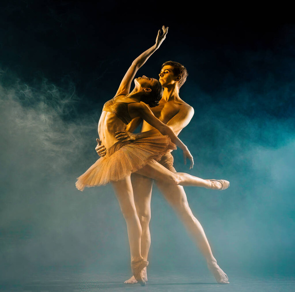 Professionele, emotionele ballet dansers op donkere scène uitgevoerd door gouden paar met body-art. Glanzende gouden huid. Paar toont liefde en passie op het podium in rook - Foto, afbeelding