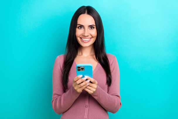 Portrait of satisfied adorable woman long hairstyle pastel clothes hold smartphone read email isolated on shine turquoise color background. - 写真・画像