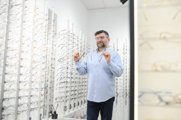 Handsome senior man choosing eyeglasses frame in optical store - Photo, image