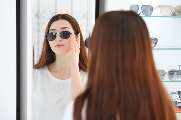 Happy Woman Wearing Sunglasses in a Optical Store. Cheerful girl trying trendy shades on sale. - Photo, Image