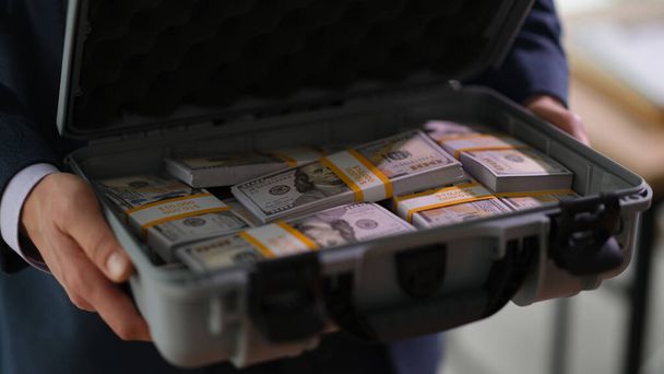 Banker holding suitcase with many dollar bills closeup. Crime and fraud giving bribe on large scale concept - Φωτογραφία, εικόνα