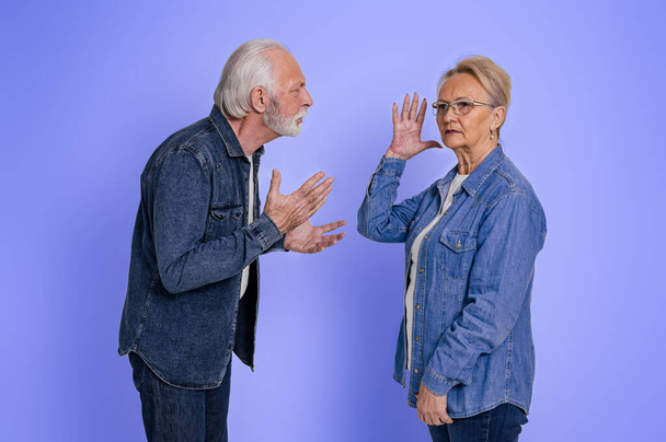 Frusztrált idős nő néz félre, és figyelmen kívül hagyja dühös férj kiabál vele, miközben a vita elszigetelt kék háttér - Fotó, kép