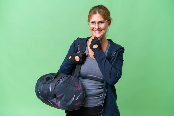Спортивная женщина средних лет со спортивной сумкой на изолированном фоне с очками и улыбкой - Фото, изображение