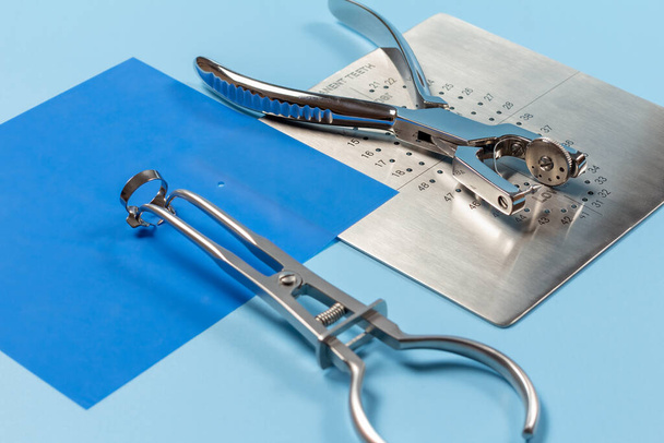 Dental hole punch, the metal plate, the rubber dam and the rubber dam forceps on the blue background. Medical tools concept. - Photo, Image