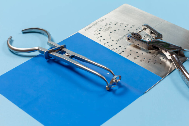 Dental hole punch, the metal plate, the rubber dam and the rubber dam forceps on the blue background. Medical tools concept. - Photo, Image