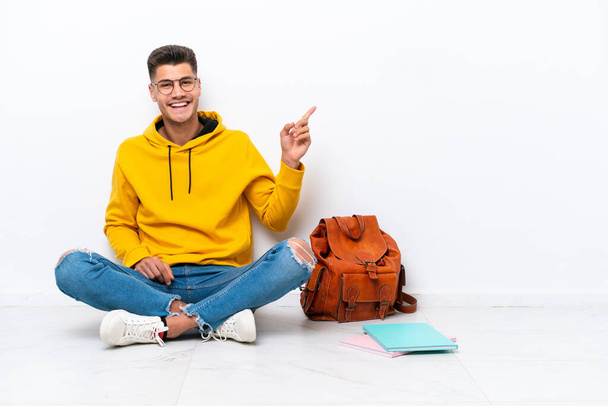 Young student caucasian man sitting one the floor isolated on white background pointing finger to the side - Photo, Image