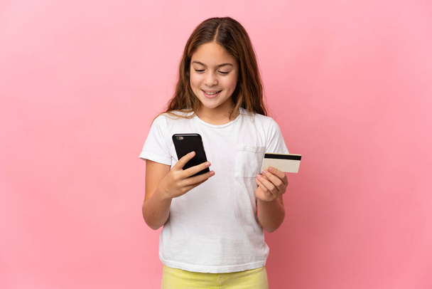 Child over isolated pink background buying with the mobile with a credit card - Foto, Bild