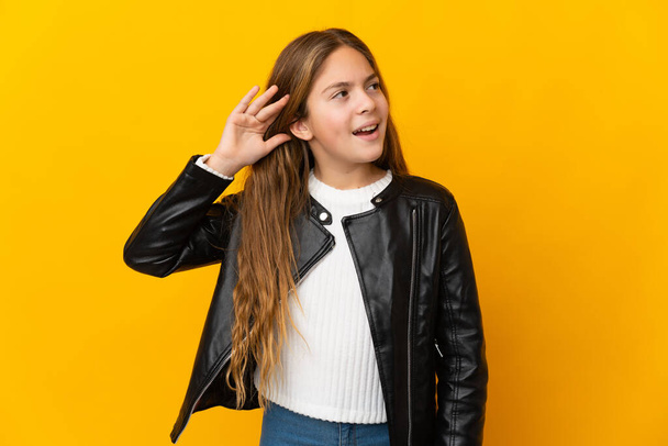 Child over isolated yellow background listening to something by putting hand on the ear - Photo, Image