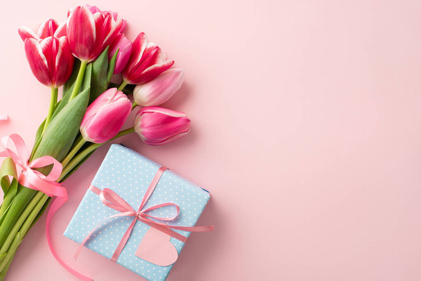 Mother's Day decorations concept. Top view photo of blue giftbox with ribbon bow and bouquet of pink tulips on isolated pastel pink background with copyspace - Фото, зображення