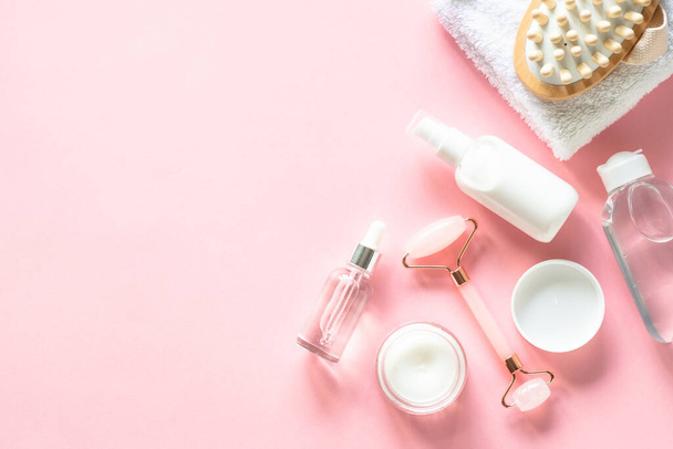 Spa products on pink. Skin care product, cream, soap serum, jade roller and white towel. Flat lay image with copy space. - Фото, зображення