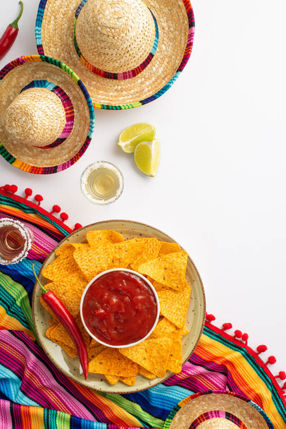 Pimentez les choses avec Cinco de Mayo inspiré vertical flat lay ! Chapeau mexicain, maracas poncho, tirs de tequila, citron vert, piments, nacho chips salsa disposés sur fond blanc pour votre message - Photo, image