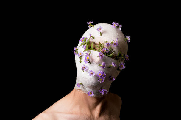 portrét chlapa s hlavou zabalenou v obvazu, z obvazu vyčnívají květiny - Fotografie, Obrázek
