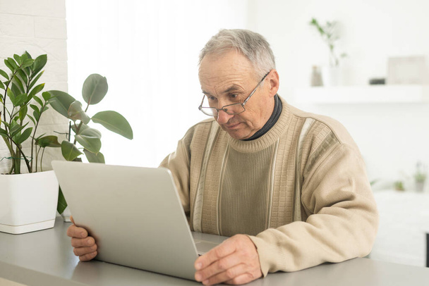 Handsome mature man in casual sitting in home office and working at laptop. - Photo, Image