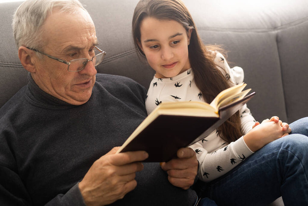 Щаслива маленька дівчинка з дідусем читає книгу історії вдома
. - Фото, зображення