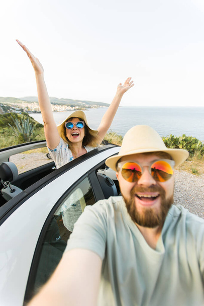 Heureux beau couple amoureux de prendre un portrait selfie au volant d'une voiture convertible sur la route en vacances. Location de voitures et concept de vacances - Photo, image