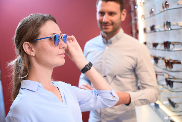 Közelkép oldalnézet portré bájos kaukázusi nő próbálja a luxus napszemüveg a férfi az optikus boltban - Fotó, kép