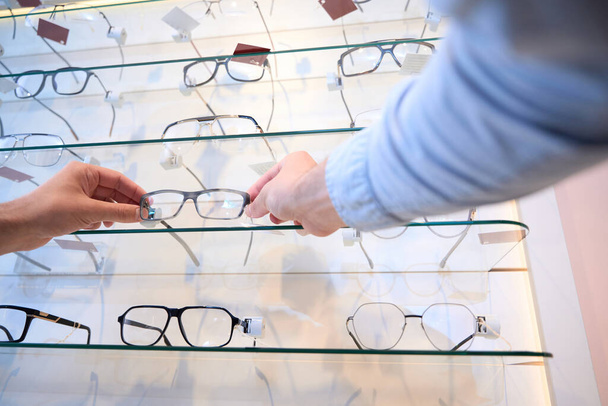 Low angle portrait of unrecognized male is selecting the optician frame in the modern shop - Photo, Image