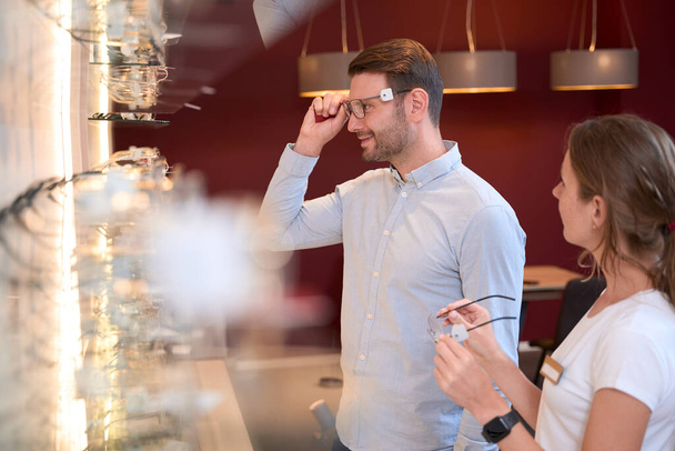 Widok z boku portret przystojnego uśmiechniętego mężczyzny nosi okulary patrząc na odbicie w luksusowym sklepie optycznym - Zdjęcie, obraz