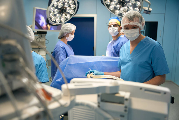 Anestesiólogo controla el flujo de medicamentos al paciente, en el fondo el cirujano con un asistente - Foto, imagen