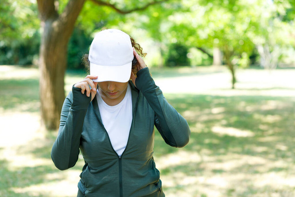 Athletic young woman wearing a white baseball cap in the woods - Фото, изображение