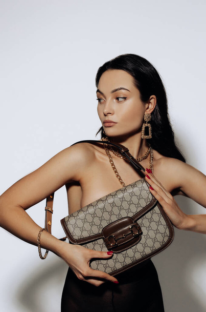 Young pretty woman poses topless and covers herself by her handbag against white background. - Photo, Image