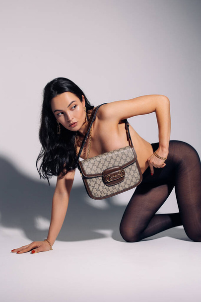 Young pretty woman poses topless in tights and covers herself by her handbag against white background. - Foto, Bild
