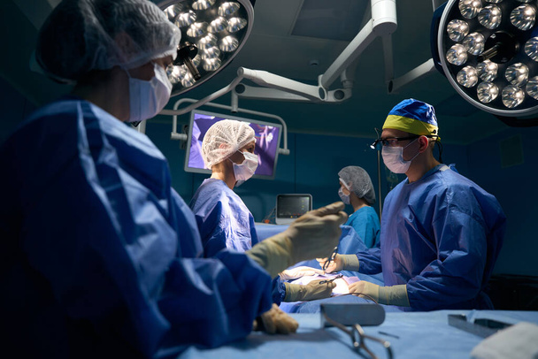 現代の手術室で患者を手術している医師のチームは、麻酔下の患者はテーブルの上にある - 写真・画像