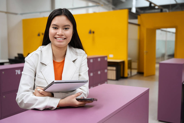 Porträt einer glücklichen Unternehmensmitarbeiterin mit Smartphone und Laptop in den Händen, die vor ihr steht - Foto, Bild