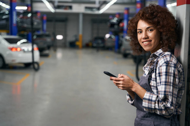 Curly pretty multiracial woman holding mobile phone in hands, repairwoman in plaid shirt - Foto, imagen