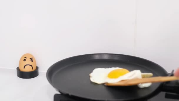 Ένα αντρικό χέρι γυρίζει ομελέτα με ένα ξύλινο ραβδί. Τηγανίζοντας ένα αυγό σε ένα τηγάνι σε λευκό φόντο - Πλάνα, βίντεο