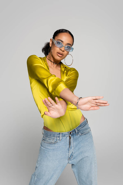african american woman in blue sunglasses and stylish outfit posing isolated on grey   - Zdjęcie, obraz