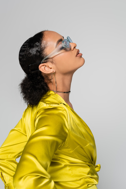 side view of african american model in blue sunglasses and stylish clothes posing isolated on grey  - Foto, Bild