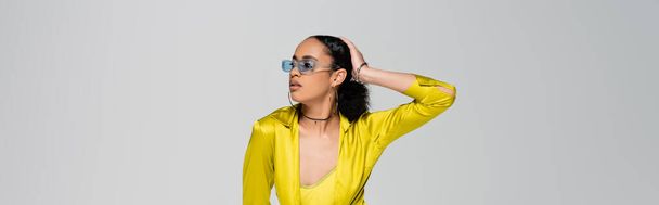 pretty african american woman in stylish sunglasses touching head while posing isolated on grey, banner  - Photo, Image