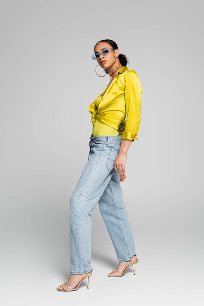 full length of stylish african american model in trendy sunglasses and high heels posing on grey  - Foto, Imagem