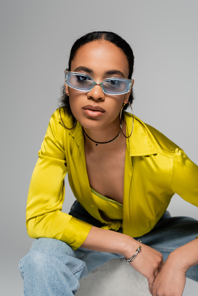 portrait of young african american model in stylish sunglasses looking at camera isolated on grey  - Foto, immagini