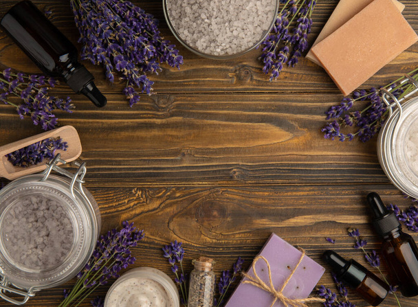 Lavender spa. Essential oils, sea salt, handmade soap, cream and body scrub with lavender flowers on brown texture wood. Natural herbal cosmetics with flowers and lavender aroma.Aromatherapy and relax. - Foto, imagen