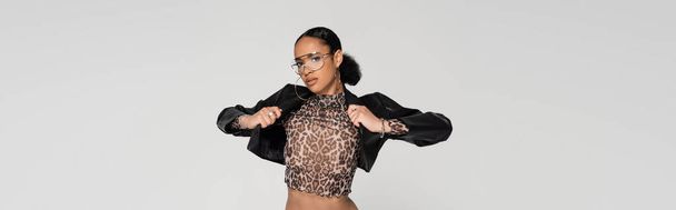 african american woman in crop top with animal print and trendy sunglasses wearing leather jacket isolated on grey, banner  - Φωτογραφία, εικόνα